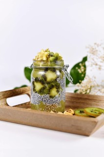 Green fruit smoothie layered in glass with chia seed pudding topped with star shaped banana and kiwi slices on wooden tray