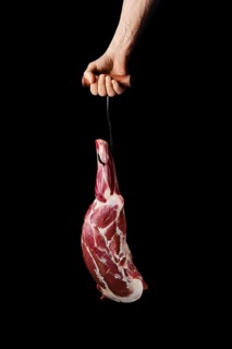 Hand of a butcher holds raw leg of lamb over black background