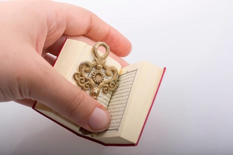 Hand holding Key and Islamic Holy Book Quran in mini size