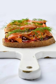 Closeup view of salmon sandwich with caramelized onion on wooden serving board
