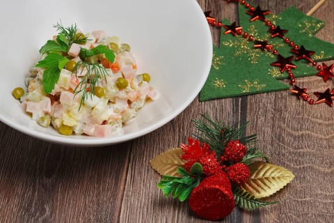 Russian traditional salad olivier with pea on wooden table near new years decorations