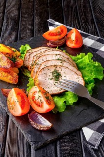 Sliced baked ham with fresh tomatoes on a stone plate in a rustic style