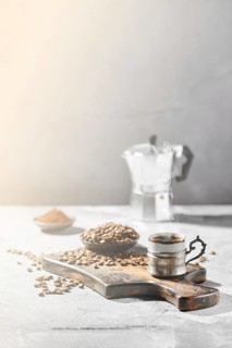Hot cup of espresso with coffee beans scattered on wooden board and a pot under hard morning sun