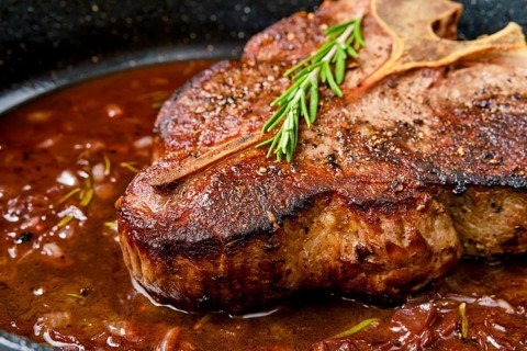 Closeup view of Porterhouse steak in wine sauce in frying pan