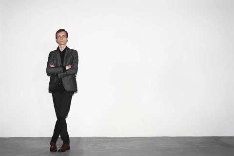 Middle age man in gray wool jacket and brown shoes standing near white concrete wall with crossed hands