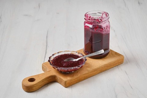 Homemade blueberry jam in a jar and saucer on wooden serving board