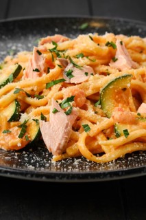 Closeup view of pasta with salmon and zuccini with grated parmesan on a plate