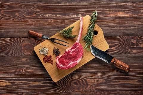 Overhead view of raw cowboy steak on wooden cutting board with spice