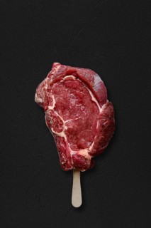 Raw beef rib steak with ice-cream stick on black background