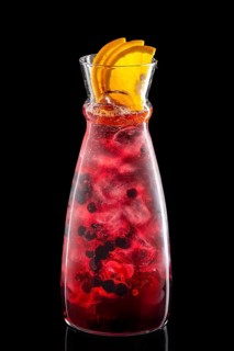 Pitcher with black currant and orange ice lemonade isolated on black background