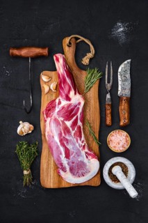 Fresh raw lamb leg bone in on wooden cutting board with herbs and seasoning