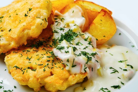 Close up view of ground chicken meat cutlet with fried potato wedges and creamy sauce with bacon on white wooden table