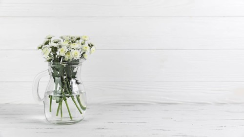 Chrysanthemum flowers inside glass jug against white wooden background