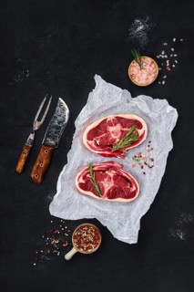 Fresh raw rack of lamb on wooden cutting board with herbs and seasoning