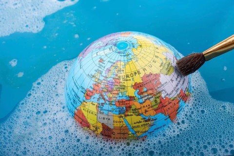 Paint brush placed on the top of globe in a water covered with foam