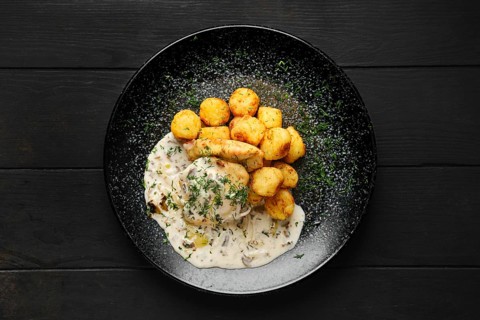 Top view of fried zander fillet with mushroom sauce and potato balls on a plate