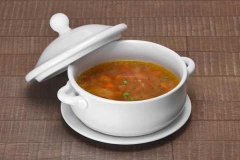 Portion of cabbage soup in ceramic pot on wooden table