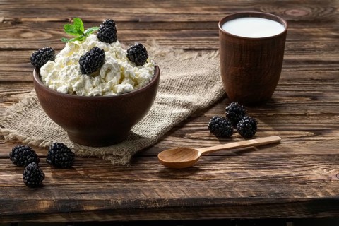 Dairy product cottage cheese and milk in brown ceramic bowl with spoon on wooden table