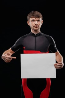 Sport. Cyclist in training clothes on black background holding blank sheet of paper. Your text here