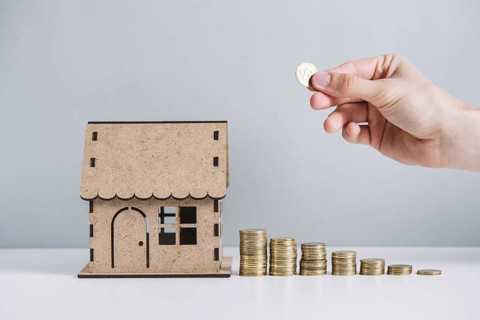 Person s hand stacking coins near house model
