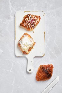Top view of assortment of fresh croissants on white serving board on marble background