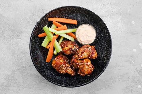 Fried chicken legs with teriyaki sauce and slices of celery and carrot on a plate