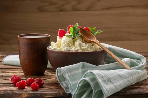 Cottage cheese with wooden spoon on it and milk in clayware on wooden table