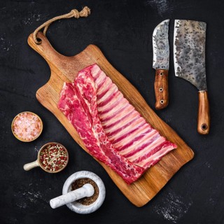 Fresh raw rack of lamb on wooden cutting board with herbs and seasoning