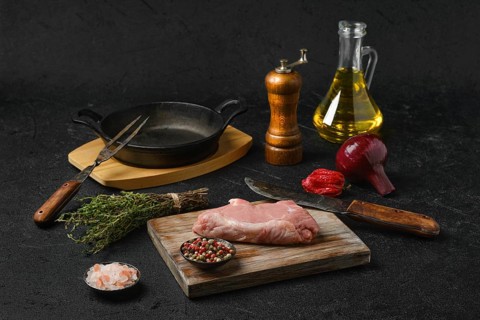 Raw veal steak bone in with ingredients for cooking on black background