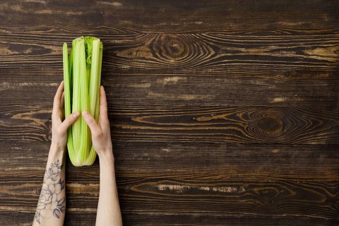 Overhead view of fresh celery in hand over wooden background