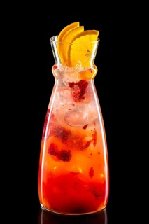 Pitcher with raspberry and orange ice lemonade isolated on black background