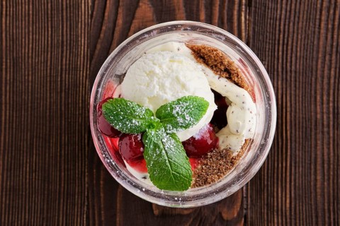Delicious tiramisu dessert with cherry in rustic pot on dark wooden background