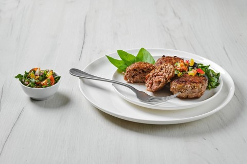 Fried veal meatballs on a plate with basil and tomato