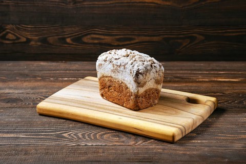 Loaf of artisan rye bread with flour topping on wooden cutting board