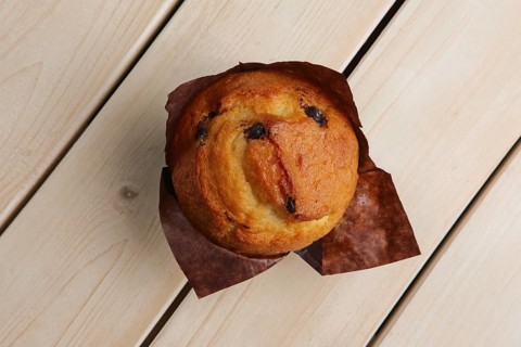 Top view of fresh muffin with chocolate chips in paper wrapper on wooden table