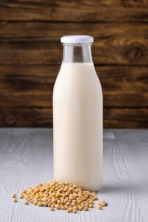 Bottle of soy milk with soybeans on white table over dark wooden background