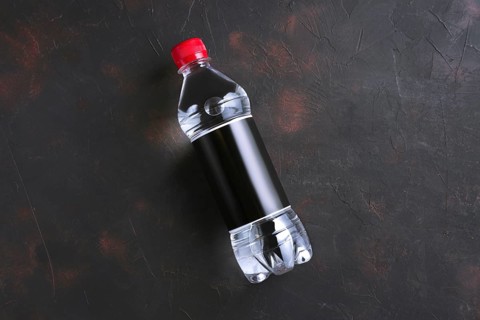 Plastic bottle of water with black label and red cap on table