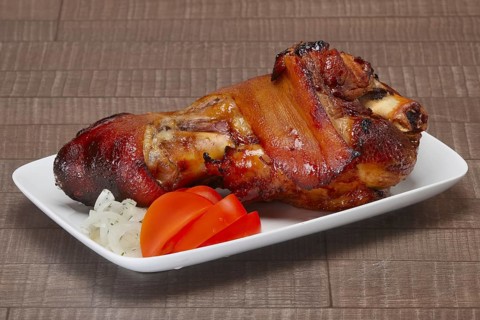 Baked pork shank with fresh slices of onion and tomato on wooden table