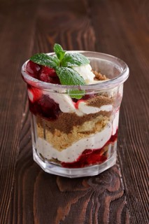Delicious tiramisu dessert with cherry in rustic pot on dark wooden background