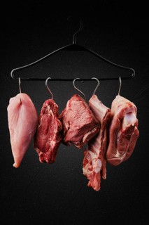 Different cuts of raw meat on hook on hanger over black background