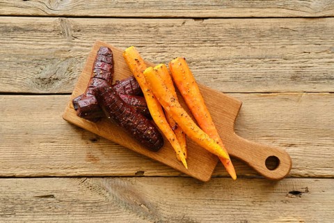 Overhead view of baked carrot and beetroot with salt and pepper on wooden board