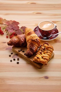 Puff pastry raisin bun and crispy croissant on wooden table with coffee
