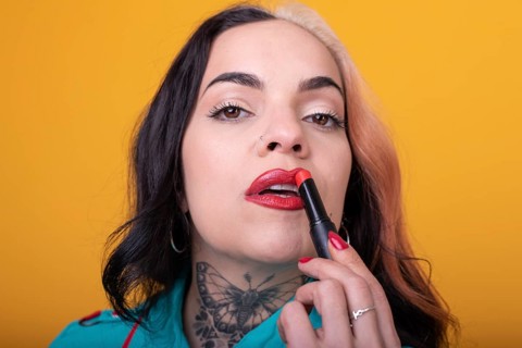Beautiful caucasian woman applying a bright red color lipstick on her lips over yellow background