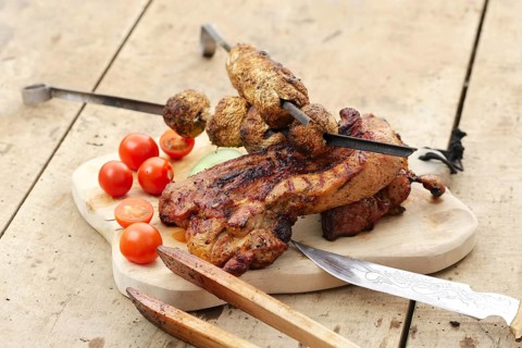 Grilled ribs and champignon on skewer served with fresh cucumber and tomato on wooden table outdoor