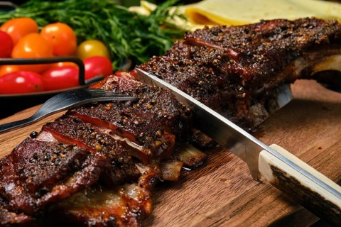 Close up view of grilled lamb breast and flap on wooden cutting board