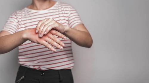 Mid section young woman having pain hand against gray background