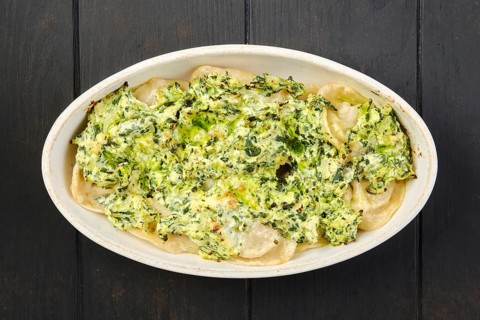 Overhead view of meat dumplings with spinach and cheese sauce baked in oven