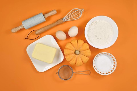 Pumpkin pie ingredients and baking tools on orange background