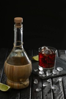 Bottle of homemade vodka and cold cocktail with lime and coffee liquor on dark background