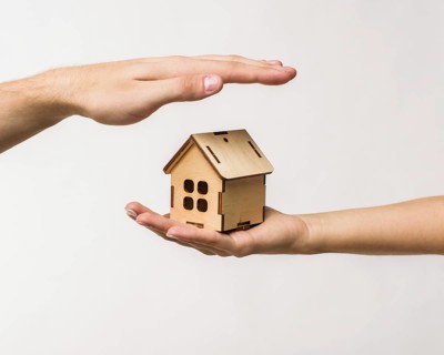 Hands protecting wooden cottage